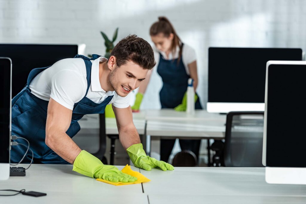 two-young-cleaners-wiping-desks-with-rags-in-offic-NWXGTZE.jpg